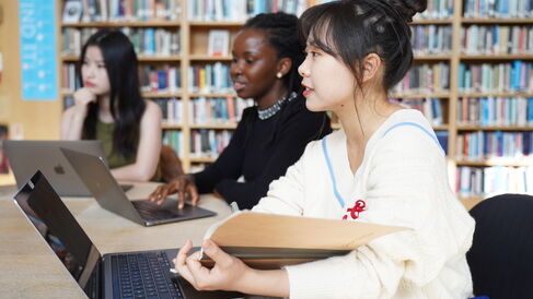 Postgraduate students seated at a library table with laptops and books