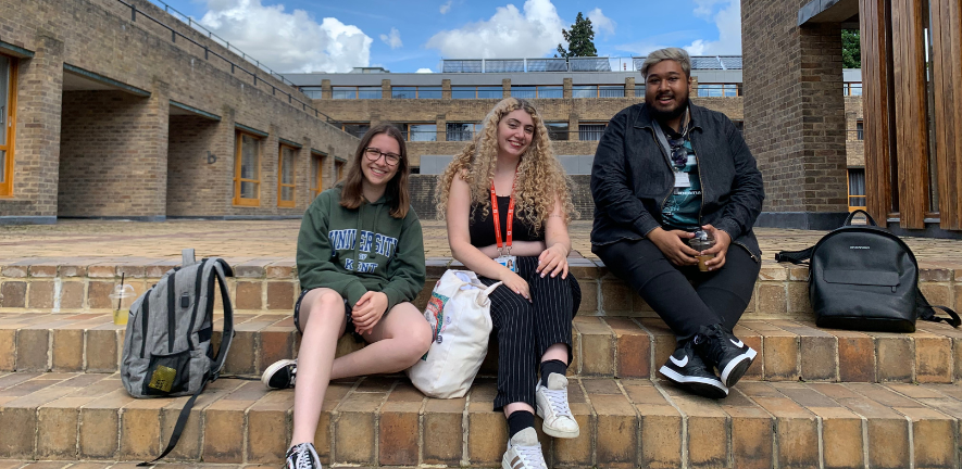 SHARE interns Farradeh, Chloe and Junad sitting on steps outside Harvey Court, postgraduate accommodation at Gonville and Caius College, Cambridge